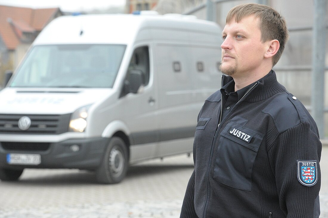 Vollzugsbediensteter vor einem Gefangenentransportauto, er schaut in die Ferne