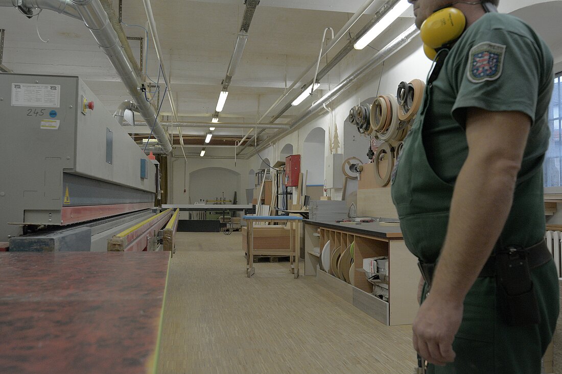 Ein Handwerksbetrieb von innen mit Werkbänken und Maschinen, im Vordergrund steht ein Mitarbeiter mit Ohrenschützern