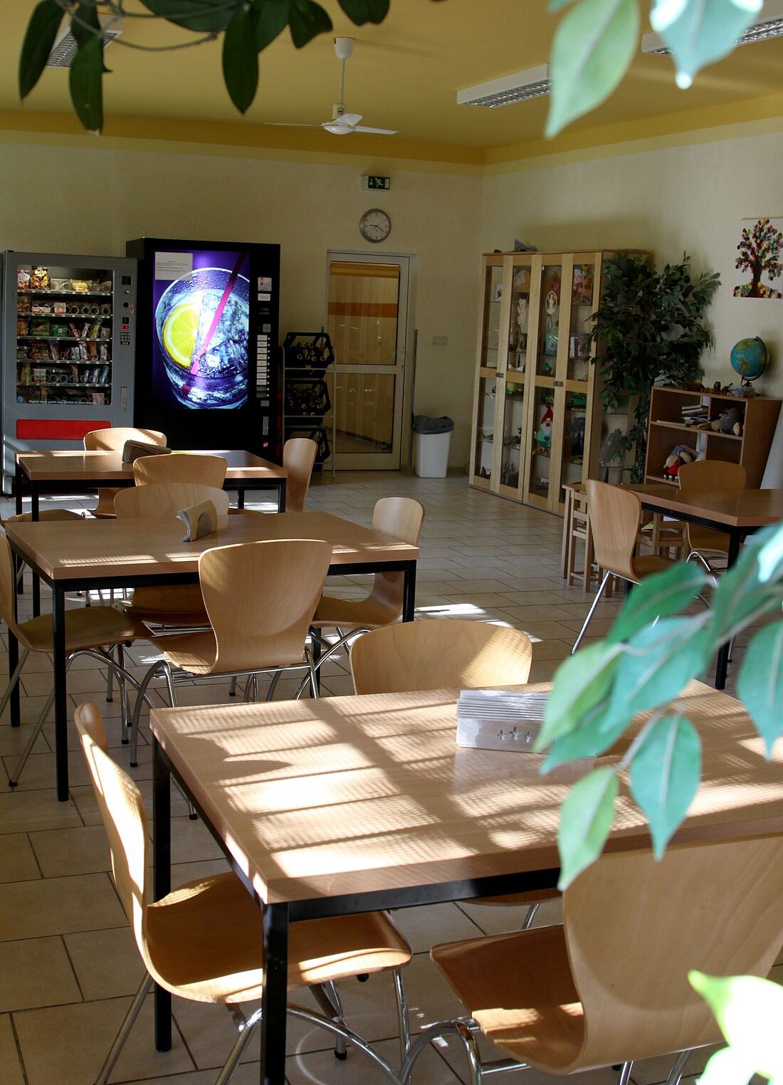 Besucherraum der JVA Hohenleuben mit Besuchertischen und Grünpflanze. Im hinteren Bereich des Raumes befinden sich Verkaufsautomaten.