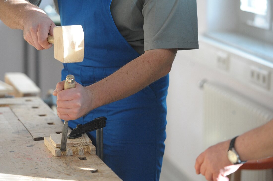 ein Mann arbeitet mit einem Holzhammer an einer Tischlerbank