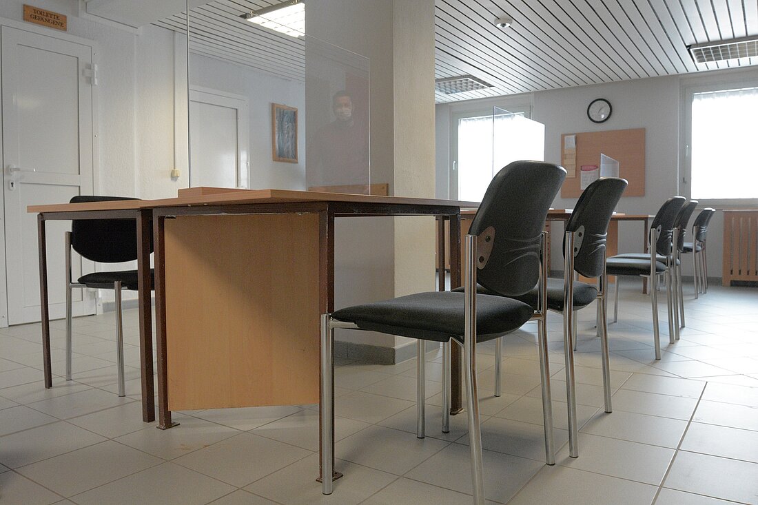 Besuchsraum mit mehreren Tischen und Stühlen und Plexiglastrennwänden in einer JVA